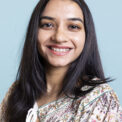 Portrait of smiling indian person posing in front of the camera, being happy and confident in herself. Upbeat friendly woman with long hair standing against blue background, freshness.