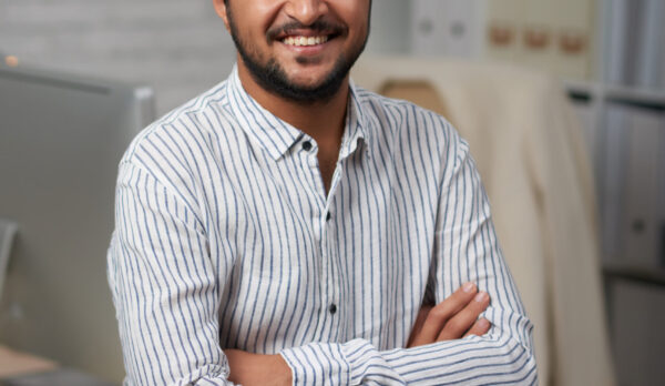 Confident young Indian businessman sitting on edge of his table and looking at camera